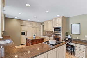 Kitchen featuring dark stone counters, built in appliances, decorative backsplash, light tile patterned floors, and cream cabinetry