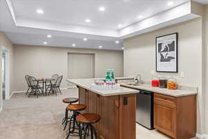 Kitchen featuring a center island, sink, stainless steel dishwasher, light stone countertops, and a kitchen bar