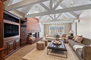 Living room with carpet, vaulted ceiling with beams, and a brick fireplace