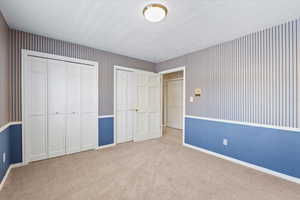 Unfurnished bedroom featuring a textured ceiling, light carpet, and two closets