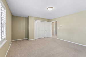 Unfurnished bedroom featuring a textured ceiling, light carpet, and a closet