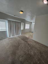 Empty room featuring a textured ceiling, light colored carpet, and an inviting chandelier