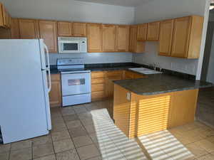 Kitchen featuring kitchen peninsula, sink, light tile patterned floors, and white appliances