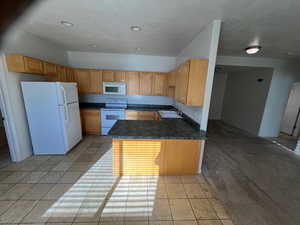 Kitchen featuring white appliances, sink, light tile patterned floors, light brown cabinetry, and kitchen peninsula