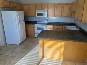 Kitchen with kitchen peninsula, white appliances, sink, and light tile patterned floors