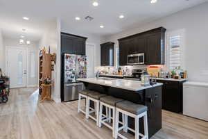 Kitchen with decorative backsplash, appliances with stainless steel finishes, light wood-type flooring, sink, and a center island with sink