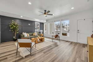 Living area with light wood-type flooring, ceiling fan, a decorative wall, and recessed lighting