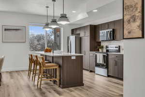 Kitchen featuring dark brown cabinetry, an island with sink, decorative light fixtures, stainless steel appliances, and a sink