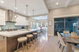 Kitchen featuring sink, wall chimney exhaust hood, decorative light fixtures, a breakfast bar area, and white cabinets