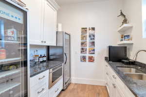 Kitchen featuring white cabinets, sink, dark stone countertops, light wood-type flooring, and stainless steel refrigerator