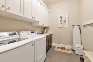 Laundry area featuring tile patterned floors, washing machine and dryer, and cabinets