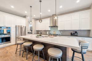 Kitchen with white cabinets, appliances with stainless steel finishes, a center island with sink, and pendant lighting