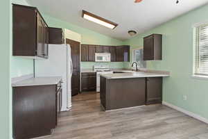 Kitchen with lofted ceiling, dark brown cabinetry, white appliances, and kitchen peninsula