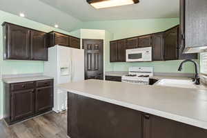 Kitchen featuring dark brown cabinetry, sink, dark hardwood / wood-style flooring, lofted ceiling, and white appliances