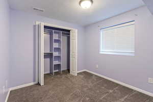 Unfurnished bedroom featuring dark colored carpet, a textured ceiling, and a closet