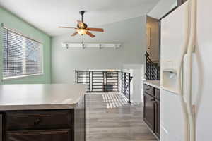 Kitchen with dark brown cabinets, ceiling fan, white refrigerator with ice dispenser, and vaulted ceiling