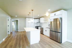 Kitchen featuring appliances with stainless steel finishes, white cabinetry, a kitchen island, and pendant lighting