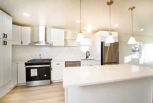 Kitchen with white cabinets, wall chimney exhaust hood, stainless steel appliances, and hanging light fixtures