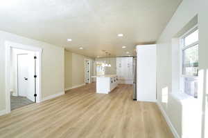 Kitchen with stainless steel fridge, light wood-type flooring, decorative light fixtures, a kitchen island, and white cabinetry