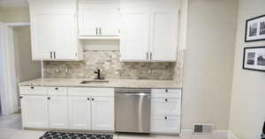 Kitchen featuring dishwasher, sink, light tile patterned floors, decorative backsplash, and white cabinets