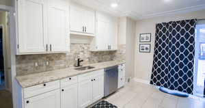 Kitchen featuring dishwasher, backsplash, sink, light stone counters, and white cabinetry