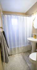 Full bathroom with toilet, shower / bathtub combination with curtain, and sink