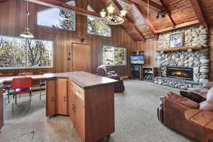 Kitchen featuring wooden walls, beam ceiling, pendant lighting, high vaulted ceiling, and a stone fireplace