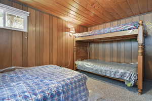 Bedroom with carpet flooring, wooden ceiling, and wooden walls