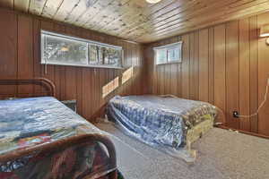 Bedroom with wooden ceiling, carpet floors, and wooden walls