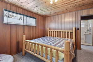 Carpeted bedroom featuring connected bathroom, wooden ceiling, and wood walls