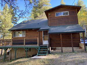 Rear view of property featuring a shingled roof, a deck, stairs, and log veneer siding