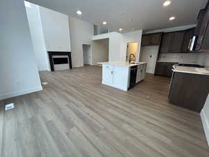 Kitchen featuring a center island with sink, sink, light wood-type flooring, black dishwasher, and tasteful backsplash