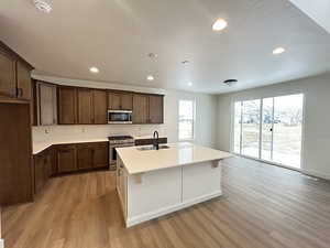 Kitchen with a center island with sink, sink, stainless steel appliances, and light hardwood / wood-style flooring