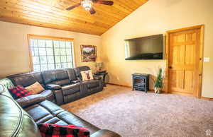 Carpeted living room featuring lofted ceiling, ceiling fan, a wood stove, and wood ceiling