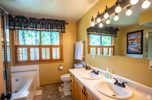 Bathroom with vanity, tile patterned flooring, toilet, a textured ceiling, and tiled tub