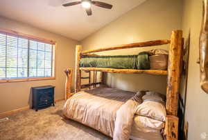 Bedroom featuring ceiling fan, a wood stove, carpet floors, and lofted ceiling