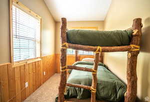 Carpeted bedroom with vaulted ceiling, multiple windows, and wooden walls