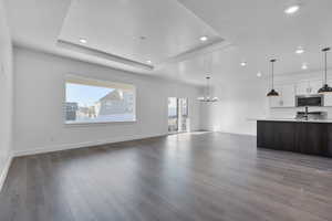 Unfurnished living room featuring dark wood-type flooring, a raised ceiling, and an inviting chandelier