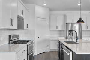 Kitchen with white cabinets, appliances with stainless steel finishes, decorative backsplash, hanging light fixtures, and light stone counters