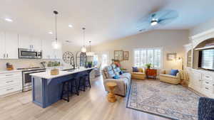 Kitchen featuring white cabinetry, stainless steel appliances, vaulted ceiling, a breakfast bar area, and a center island with sink