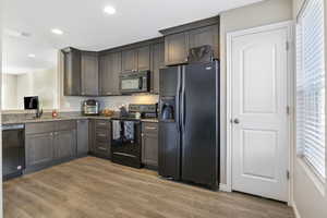 Kitchen with black appliances, sink, dark stone countertops, light wood-type flooring, and dark brown cabinetry