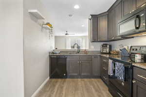 Kitchen featuring black appliances, sink, dark stone counters, and light hardwood / wood-style flooring