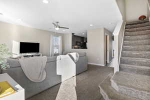 Living room with ceiling fan and dark colored carpet