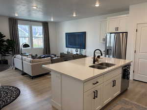 Kitchen with light wood-type flooring, stainless steel appliances, sink, white cabinetry, and an island with sink