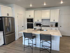 Kitchen with white cabinets, stainless steel appliances, hardwood / wood-style flooring, and an island with sink