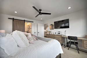 Carpeted bedroom featuring a barn door and ceiling fan