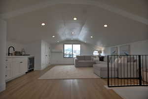 Living room featuring vaulted ceiling, indoor bar, light hardwood / wood-style flooring, an AC wall unit, and wine cooler