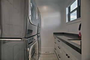 Washroom featuring stacked washer / dryer, tile patterned flooring, cabinets, and sink