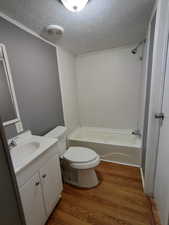 Full bathroom featuring washtub / shower combination, hardwood / wood-style floors, a textured ceiling, toilet, and vanity