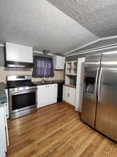 Kitchen with backsplash, vaulted ceiling, light hardwood / wood-style floors, white cabinetry, and stainless steel appliances